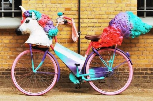 A unicorn sculpture mounted on a bicycle with pink, purple and blue paint.